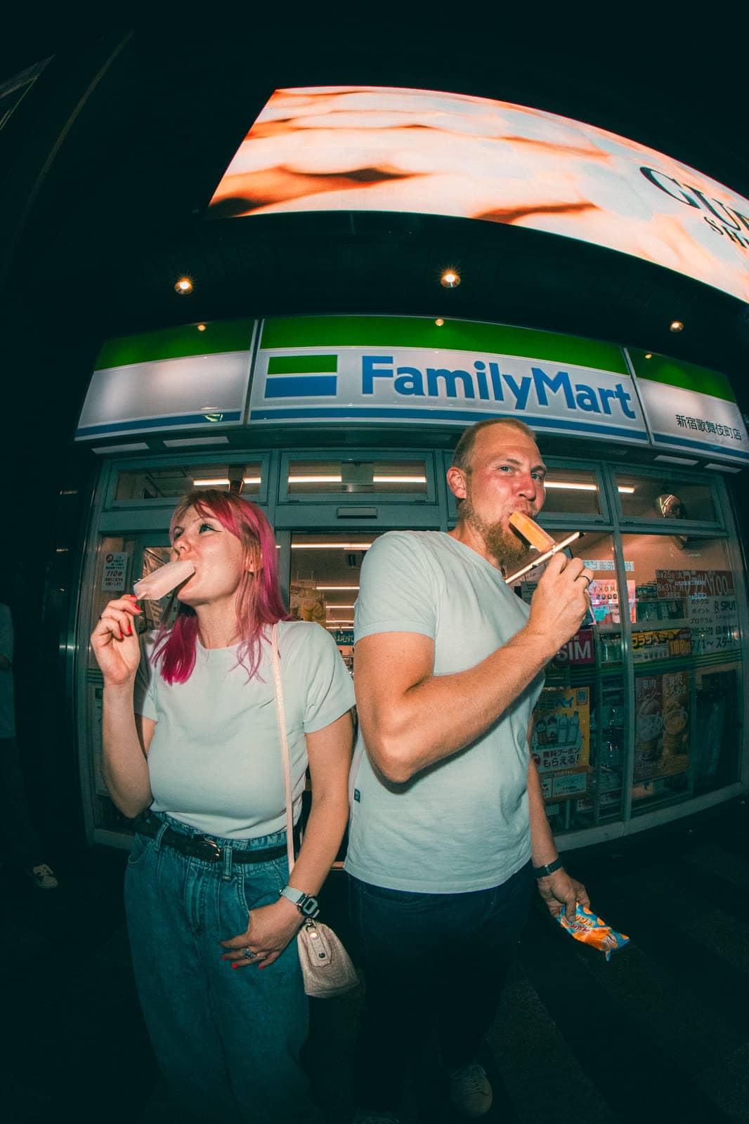 Couple eating snacks outside a convenience store at night