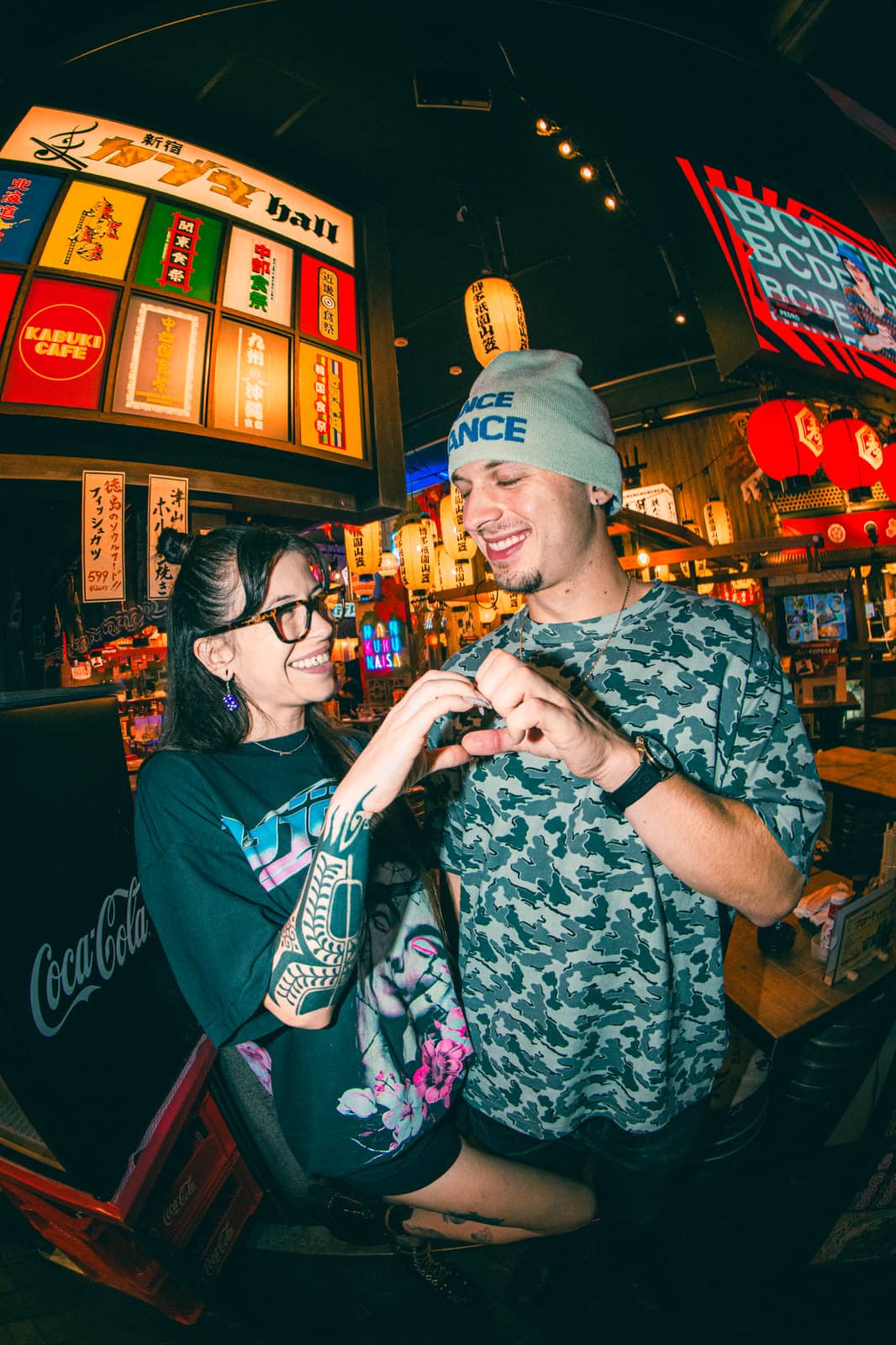 Couple making a heart with their hands under neon signs