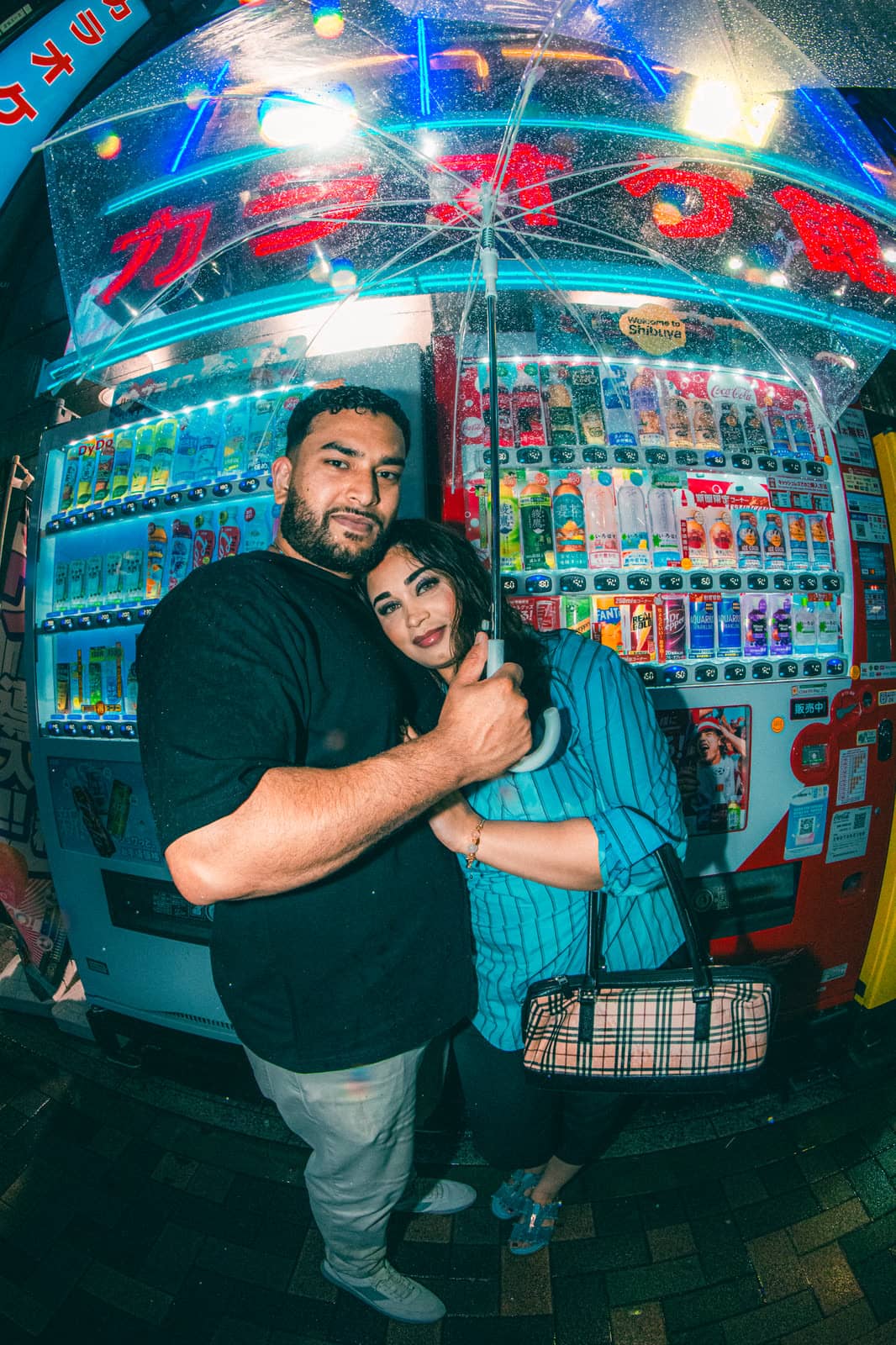 Couple under a clear umbrella at a vending machine at night