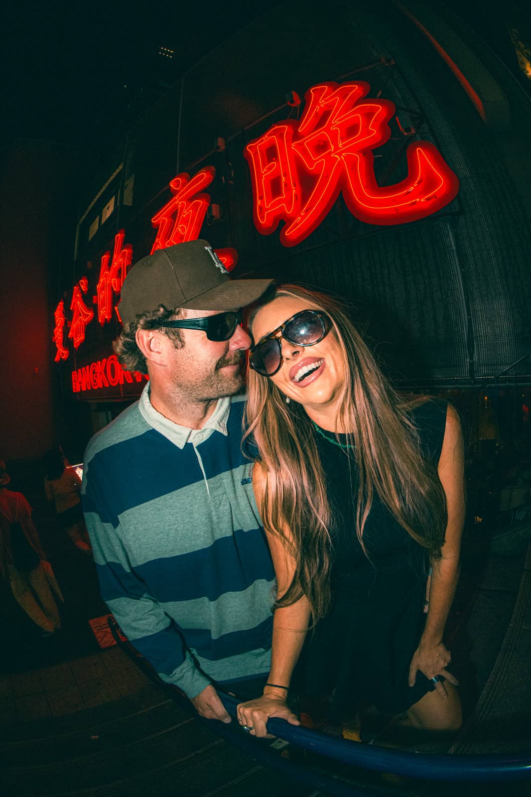 Couple in sunglasses under a red neon sign at night