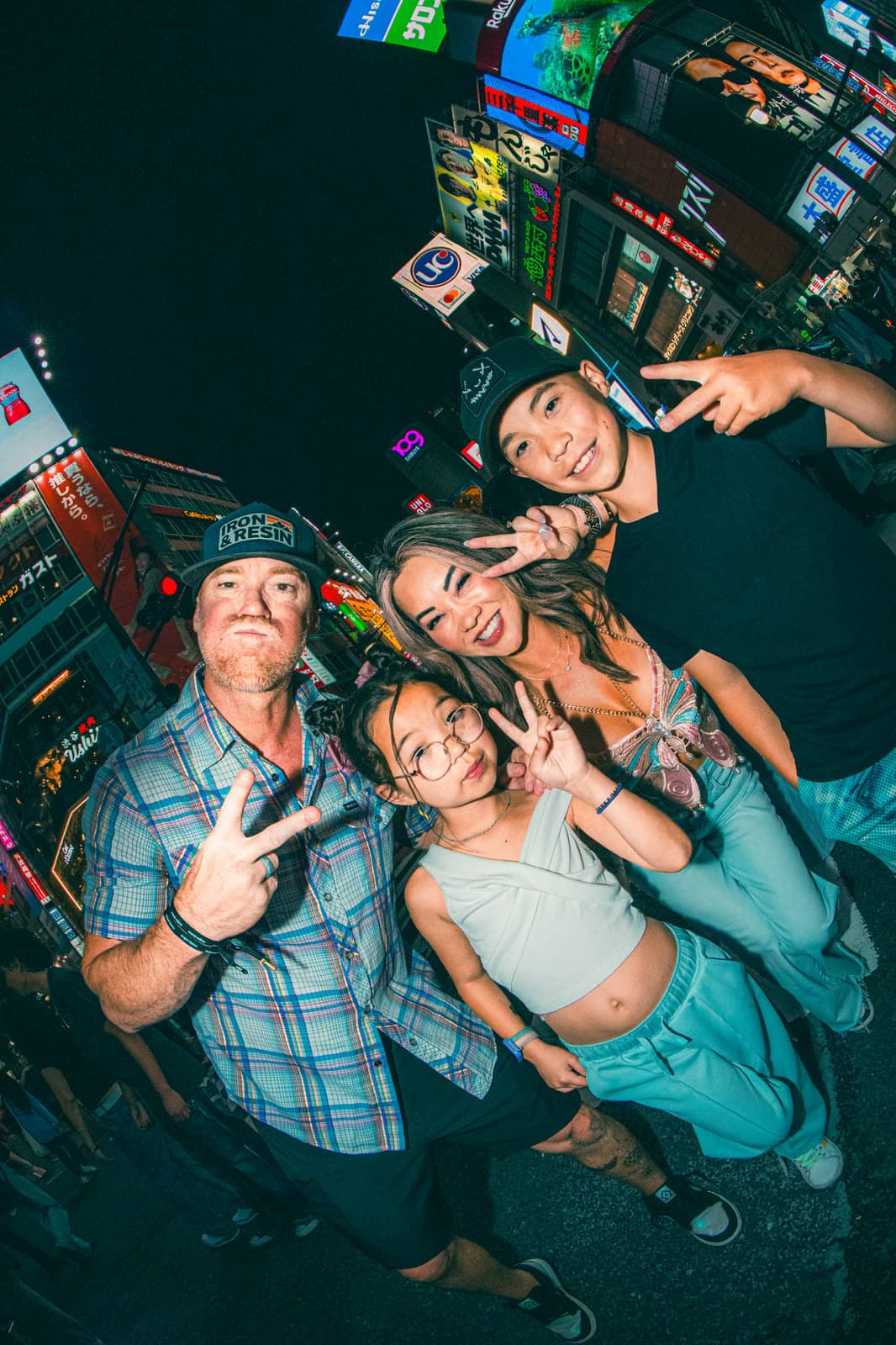 Family making peace signs on a neon street at night