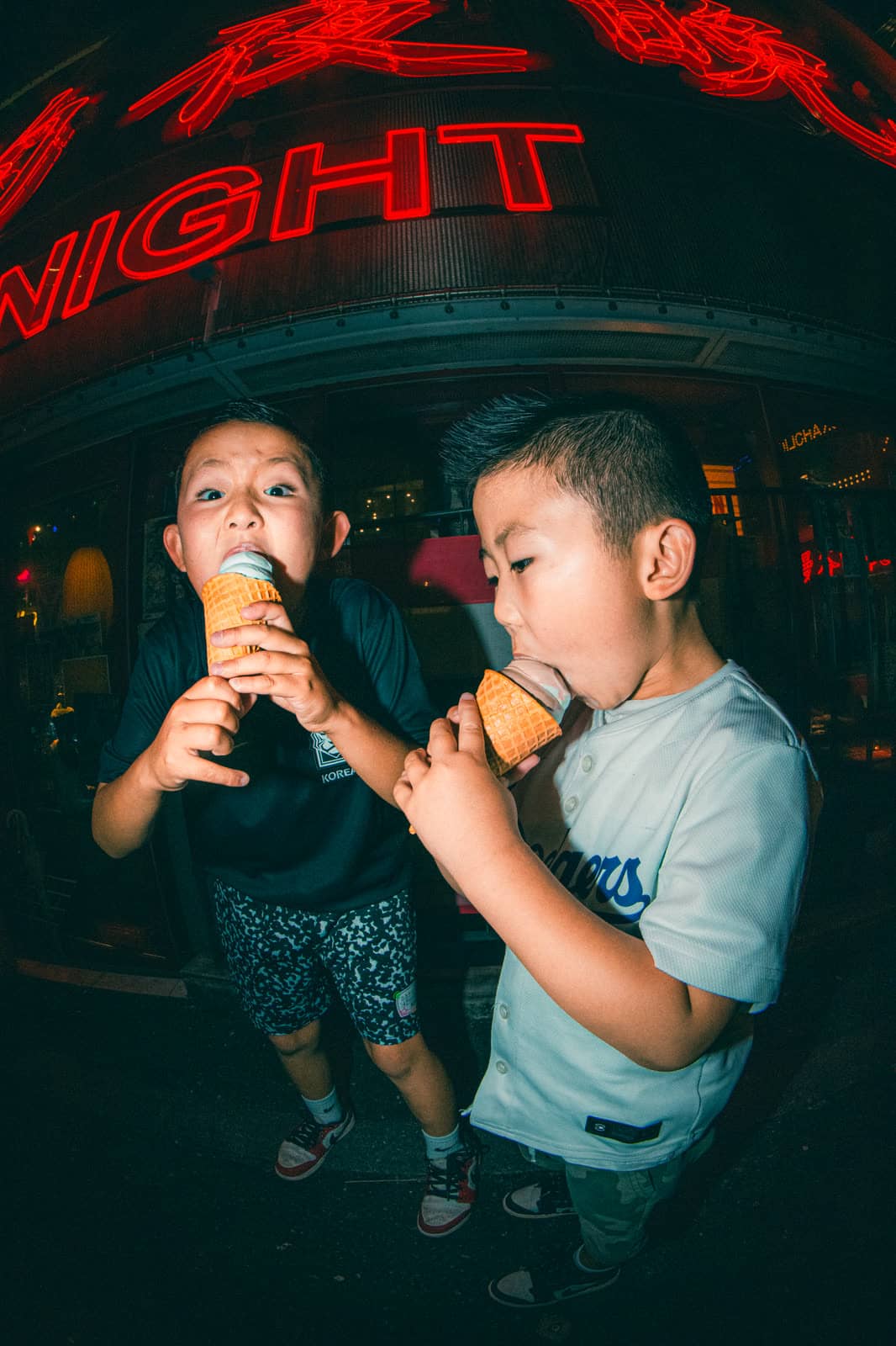 Two boys eating ice cream under a red neon sign