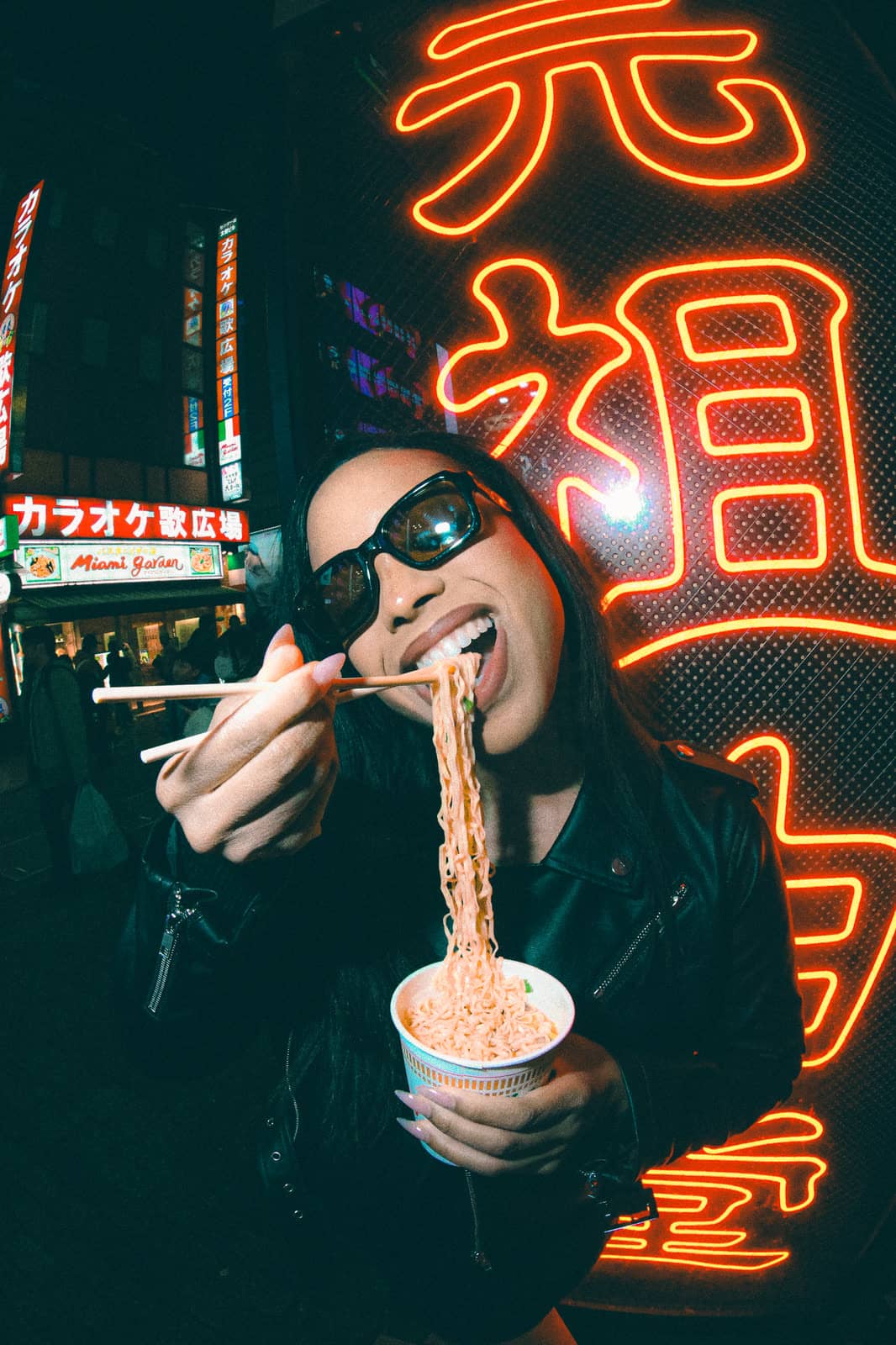 Woman eating noodles under a red neon sign